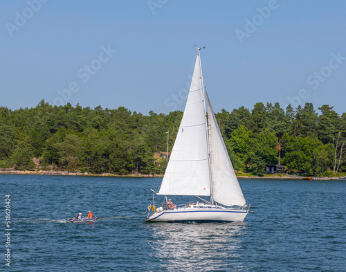 Sailing boat pulling a rubber raft at an open bay in the archipelago a sunny summer day in Stockholm