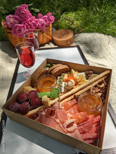 Box with tasty snack and glasses with wine on summer picnic with wooned box and flowers on background.