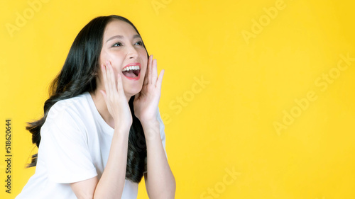 beautiful Asian young woman screams announce the good news or promotion , holding hands near her face with open mouth Herald news promotion isolated on yellow background