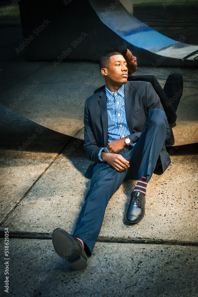 Tired. Young black businessman, sitting on ground, leaning against mirror wall on street in New York City, relaxing, thinking..