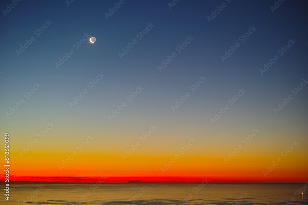 Peaceful ocean landscape at sunset over a calm empty sea at dawn. Wallpaper of stunning red and yellow light reflecting on the water from the midnight sun at twilight dusk with copy space background