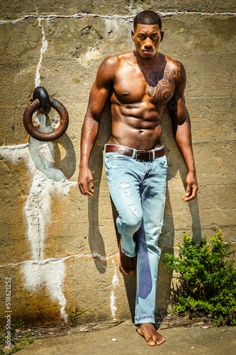 Obraz na płótnie Summer Heat. Masculine black man wearing blue jeans, barefoot, half naked, standing against wall with metal ring, under sunshine, looking forward.. w salonie