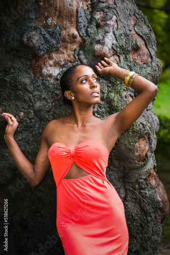 Obraz na płótnie By the tree, Young woman wearing red two pieces dress, standing by old tree trunk, looking around, wondering. w salonie
