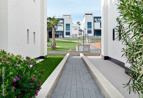 Narrow footpath along two white residential houses path leading to inner yard of similar townhouses