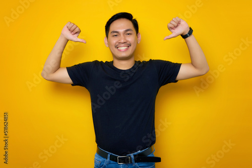 Cheerful young Asian man in casual t-shirt pointing at herself with proud isolated on yellow background. People lifestyle concept © Bangun Stock Photo