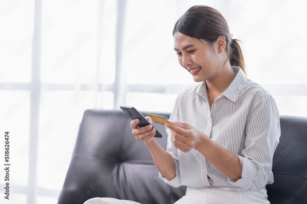 Cropped shot smiling young Asian woman using a credit card and shopping online payment on smartphone at home. Cropped shot smiling young Asian woman using a credit card and shopping online payment on smartphone at home.