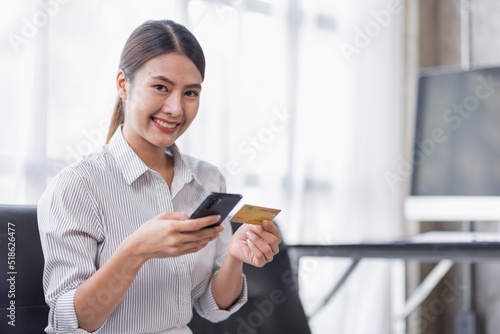 Cropped shot smiling young Asian woman using a credit card and shopping online payment on smartphone at home.