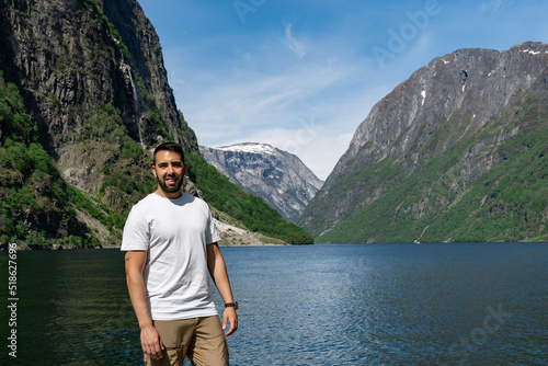 Young male tourist in the foreground and behind him the high mountains and the fjord, in Gudvangen - Norway