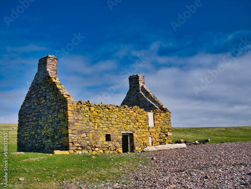 An abandoned, derelict croft or farm house with no roof on a pebble beach at Stenness, Northmavine in  Shetland, Scotland, UK. Yellow lichen grows on the walls. photo