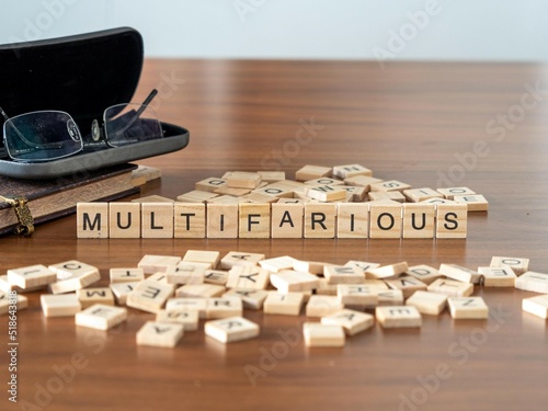 multifarious word or concept represented by wooden letter tiles on a wooden table with glasses and a book