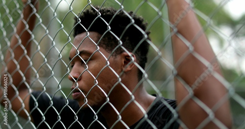 Pensive black guy leaning on security metal fence © Marco