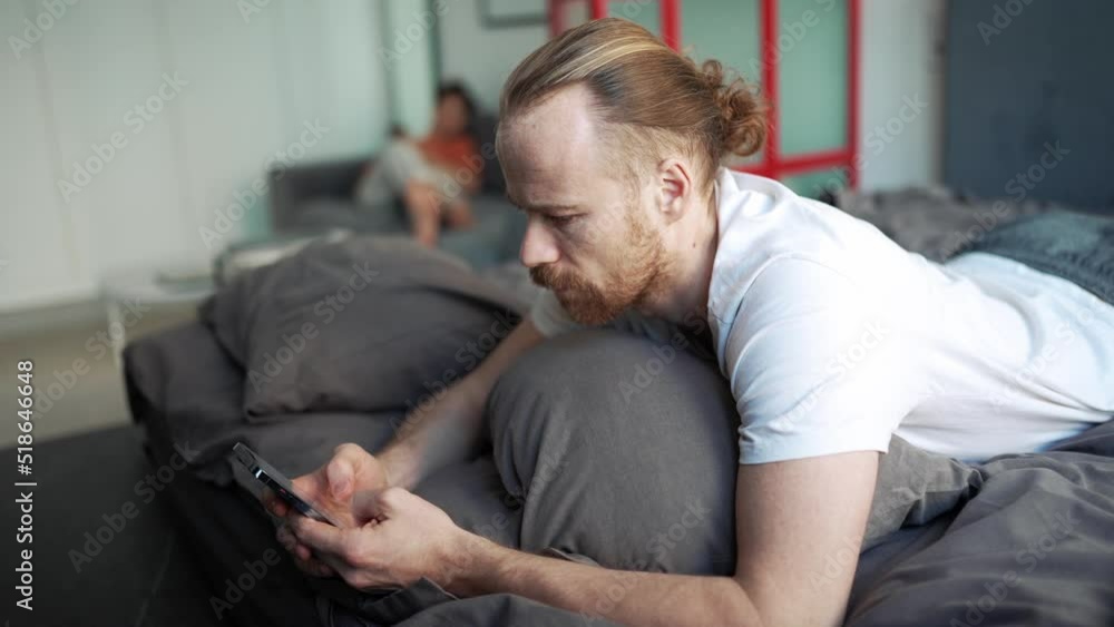 Serious bearded man texting on mobile while lying on the bed at home Serious bearded man texting on mobile while lying on the bed at home
