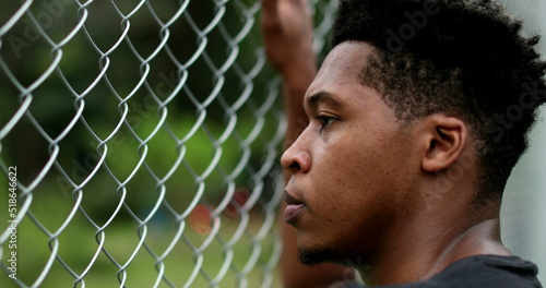 Pensive angry young black man leaning on metal fence outside thinking © Marco