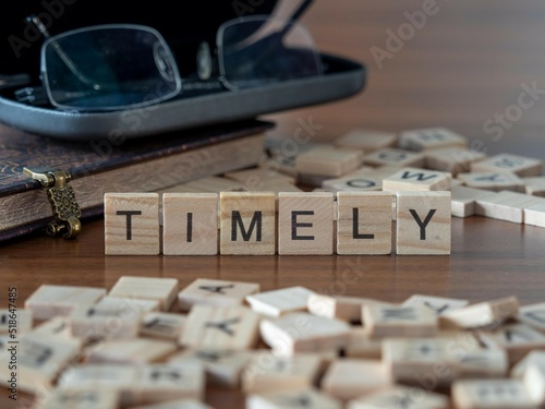 timely word or concept represented by wooden letter tiles on a wooden table with glasses and a book