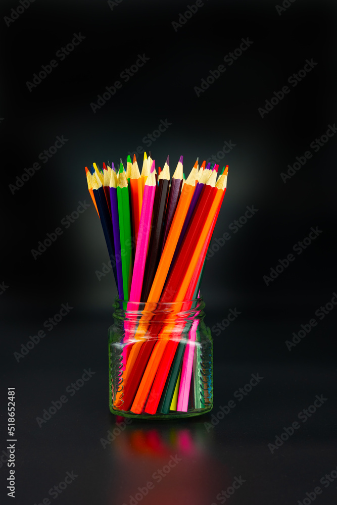 Many colored pencils in a glass on black background