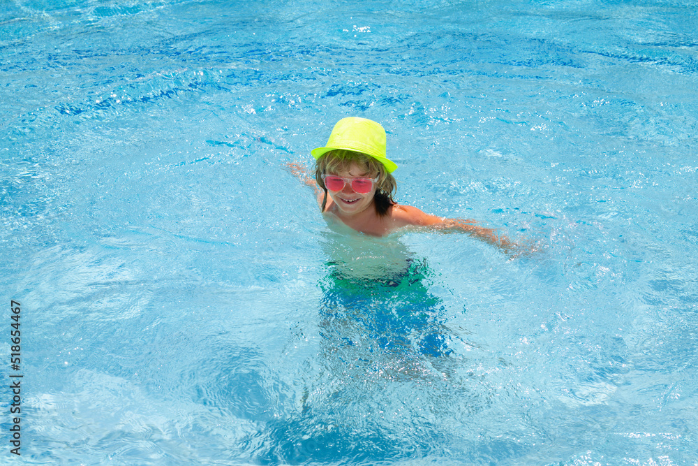 Kid boy playing in swimming pool. Fashion summer kids in hat and pink sunglasses. Child splashing in swimming pool.