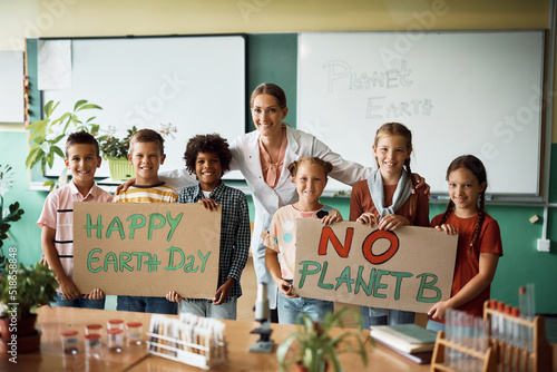 Happy science teacher and school children who are holding placard with 'Happy Earth day' and 'No planet B' message in classroom. © Drazen