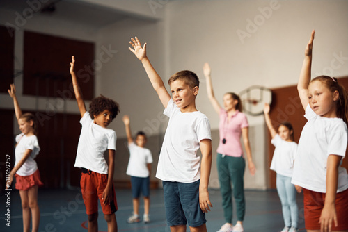 Group of elementary students with raised arms exercising on PE class at school gym. © Drazen