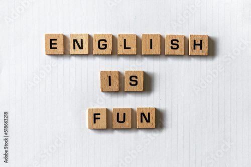 Wooden letters spell out 'English is fun' on a blank white lined notepad. Hardwood desk surface. Back to school, in-person learning, online learning, studying, no people, literacy, primary school.