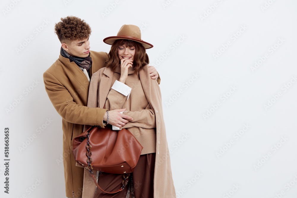 a beautiful, loving couple of a man and a woman stand on a white background in stylish autumn clothes, gently embracing and the woman joyfully holds her hand near her face
