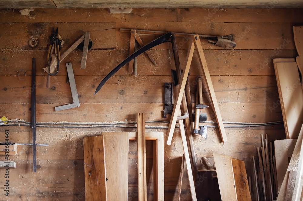 Wall in the carpentry workshop with many tools and planks of wood, as well as some hand tools. Rustic workshop. Wall in the carpentry workshop with many tools and planks of wood, as well as some hand tools. Rustic workshop.