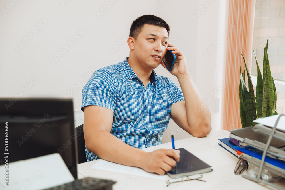 a young Asian businessman is talking on the phone to discuss work in the office. the man is Asian. a young Asian businessman is talking on the phone to discuss work in the office. the man is Asian.