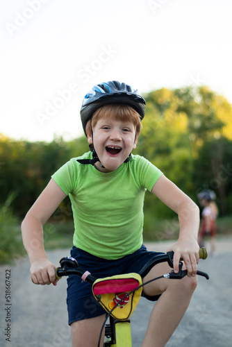 Close-up of a laughing teenager boy in helmet and green T-shirt looking at camera riding a bicycle on the road in the countryside in summer