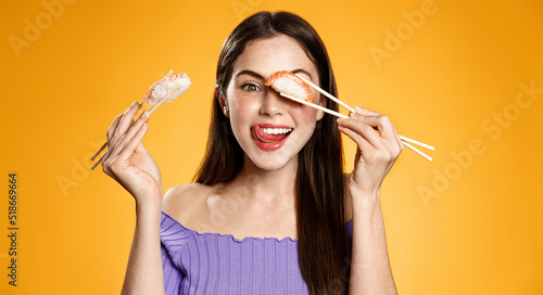 Happy woman with asian food. Girl with chopsticks eats sushi rolls and nigiri, order take out delivery, orange background