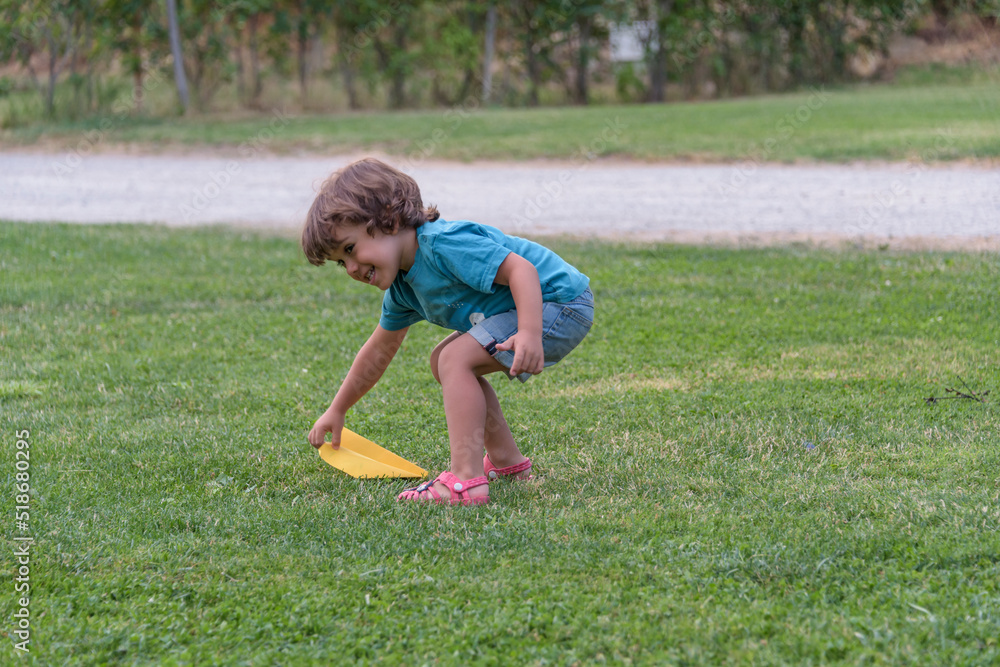 Boy playing toss paper plane outdoors looking away. Portrait of a cheerful caucasian boy playing in the spring and summer park having fun on the weekend. Boy playing toss paper plane outdoors looking away. Portrait of a cheerful caucasian boy playing in the spring and summer park having fun on the weekend.