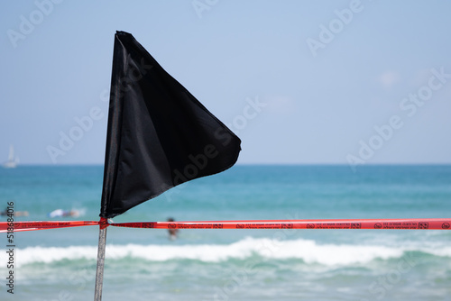 Black flag with a red ribbon on the sea shore warning about dangerous current and waves or invasion of jellyfish.