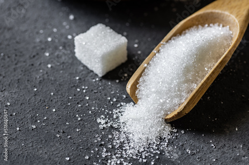 Heap of white granulated sugar in spoon with sugar cube