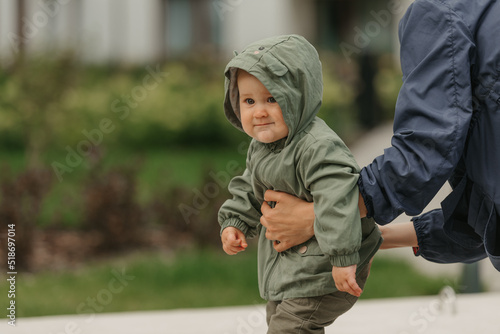 Obraz na płótnie A close photo of a female toddler who is held by her mom in the street at noon. A mother is teaching her young daughter how to do steps near their home on a cloudy day. w salonie