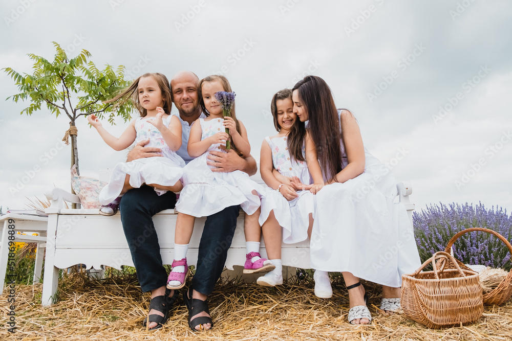 Fototapeta premium Family sitting on the picnic blanket in city park during weekend Sunday sunny day. Children are having fun playing.Happy cheerful family in nature, weekend.A plantation of blue flowers