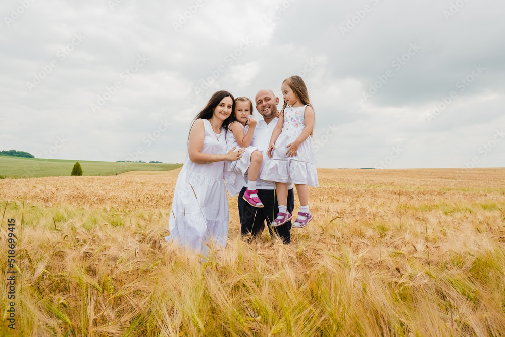 A mother and her daughter are having fun in a wheat field. Smiling dad in a White shirt enjoying time with little  daughter in summer day.