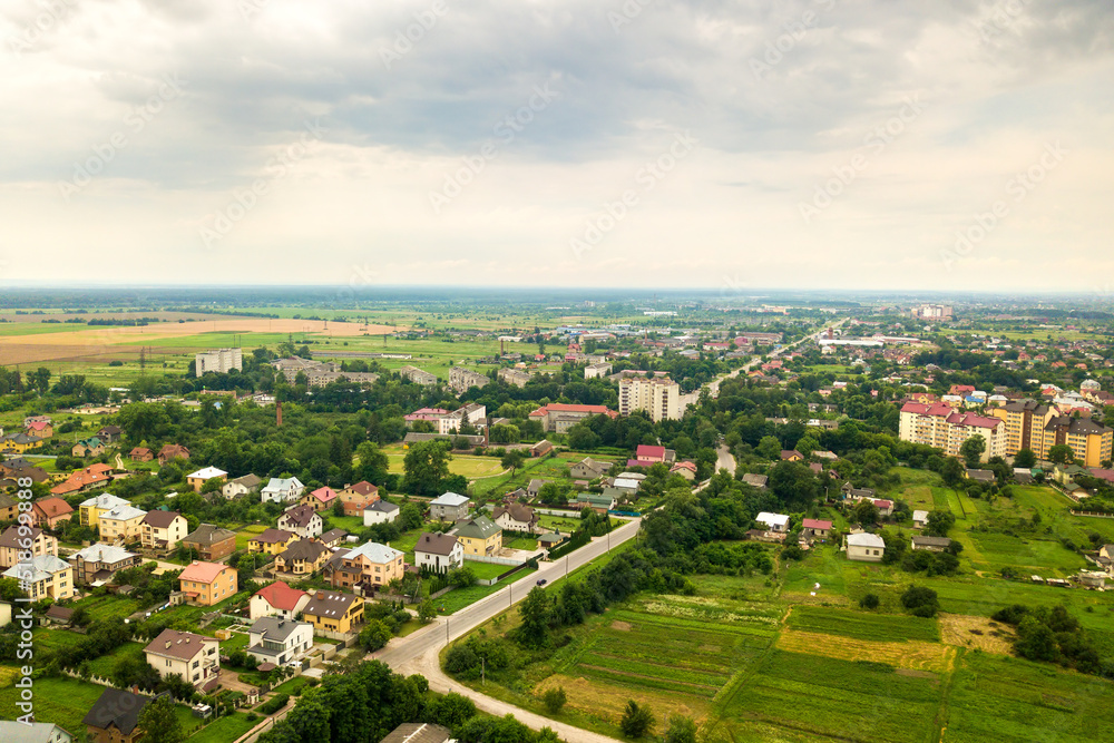 Aerial landscape view of village houses and distant green cultivated agricultural fields with growing crops on bright summer day