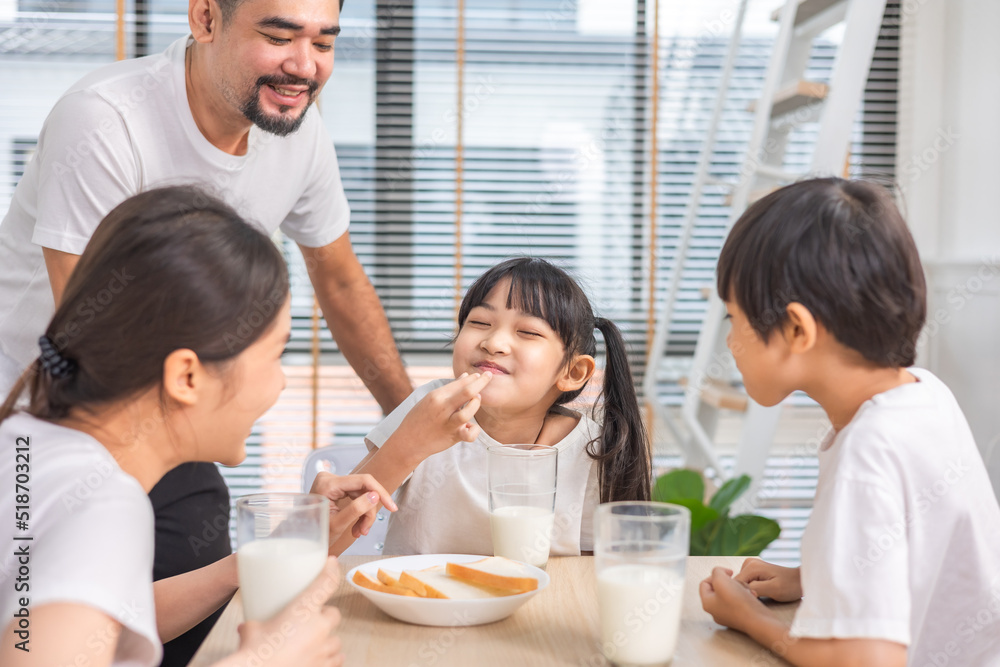 Asian family enjoying breakfast at living room. little girl daughter sitting on table, drinking milk with smiling father and mother in morning. Happy family at home. Asian family enjoying breakfast at living room. little girl daughter sitting on table, drinking milk with smiling father and mother in morning. Happy family at home.