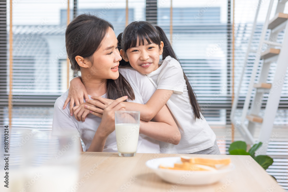 Asian  family enjoying breakfast at living room. little girl daughter sitting on table, drinking milk with smiling father and mother in morning. Happy family at home.