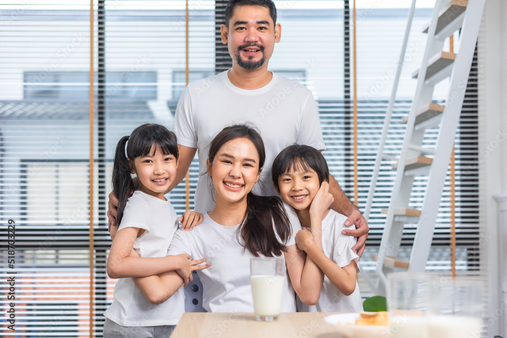 Obraz premium Asian family enjoying breakfast at living room. little girl daughter sitting on table, drinking milk with smiling father and mother in morning. Happy family at home.