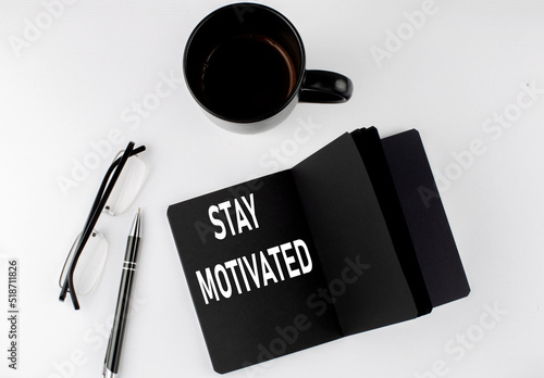 STAY MOTIVATED written text in small black notebook with coffee , pen and glasess on white background. Black-white style