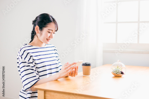 家のテーブルでスマホを使う日本人女性（アプリ・笑顔） 