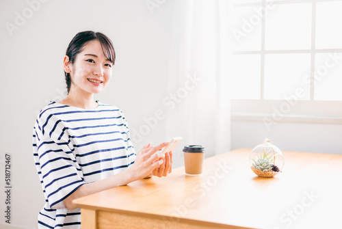 家のテーブルでスマホを使う日本人女性（アプリ・笑顔）
