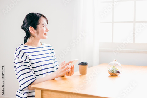 家のテーブルでスマホを使う日本人女性（アプリ・笑顔） 