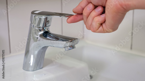 Strong male hand opens water faucet. Water stream flows from tap. Clear water runs quickly and man forgets to turn off water closeup photo