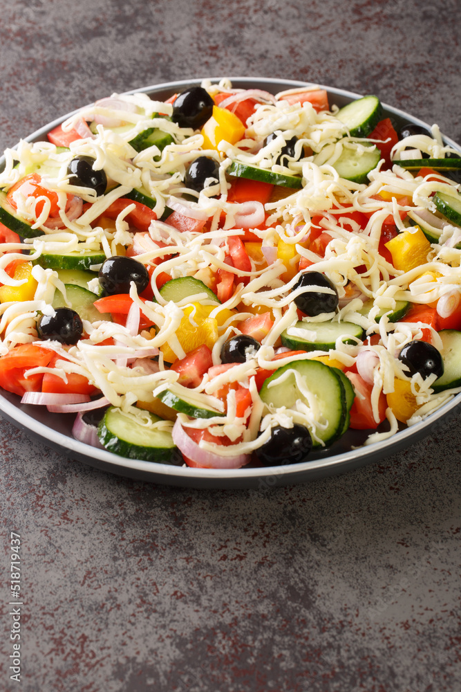 Shopska salad with tomatoes, cucumbers, onions, bell peppers, olives and cheese close-up in a plate on the table. Vertical