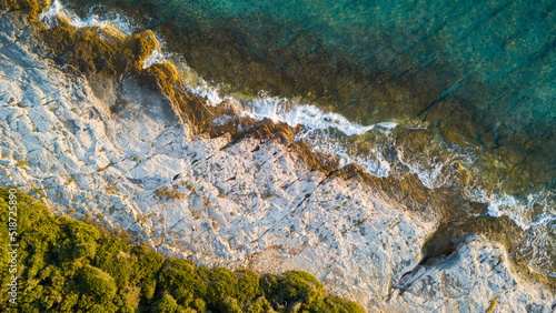 Aerial drone view of sea and rocks on the beach. Beautiful natural rocky beach at summer. Waves crushing on wild beach at sunset. Coastline. Transparent sea water