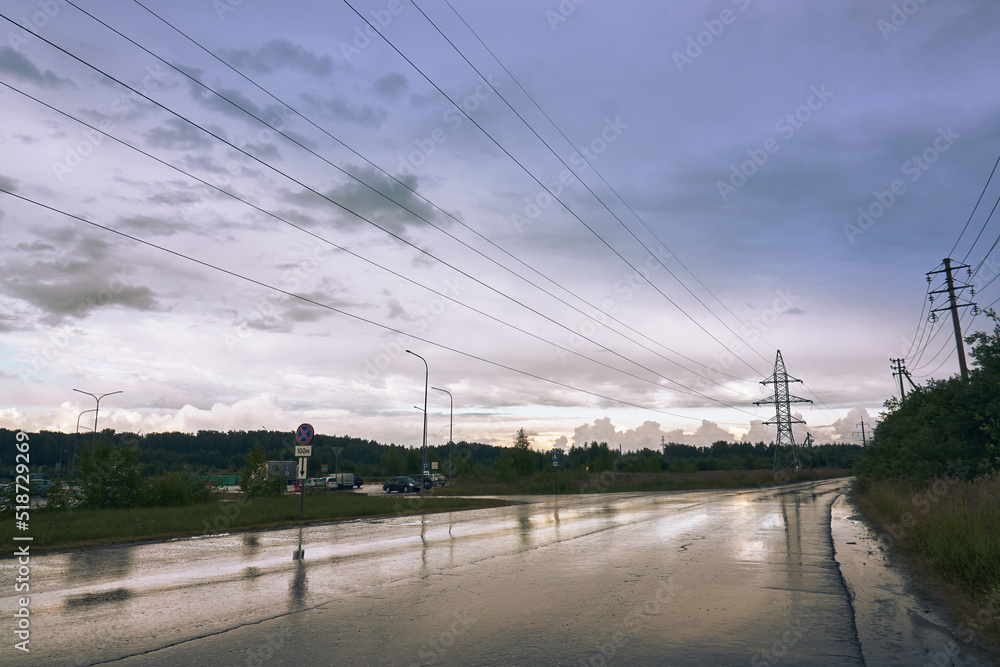 Summer evening scenery, beautiful evening blue sky, wet aswalt, high-voltage line running along the road, poles with wires, countryside