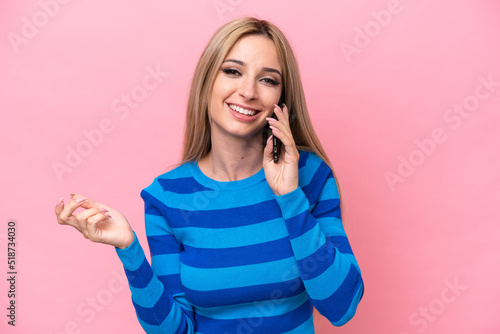 Pretty blonde woman isolated on pink background keeping a conversation with the mobile phone with someone