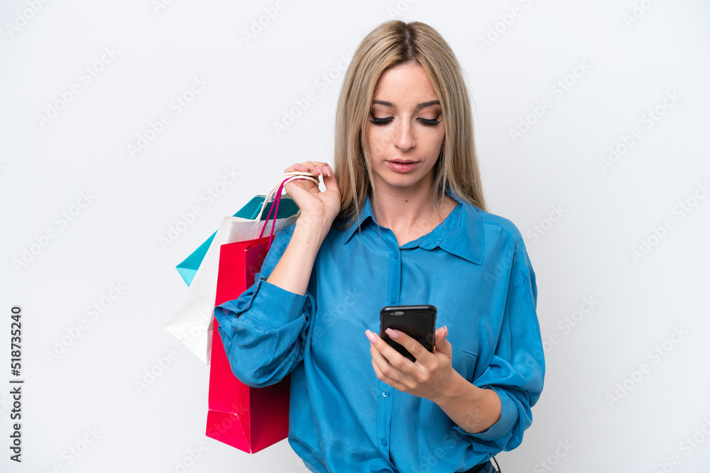 Pretty blonde woman isolated on white background holding shopping bags and writing a message with her cell phone to a friend Pretty blonde woman isolated on white background holding shopping bags and writing a message with her cell phone to a friend