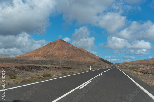 Una carretera vacía con un volcán al fondo en Lanzarote, Islas Canarias. Desierto árido con una carretera de doble sentido con un ambiente seco.  