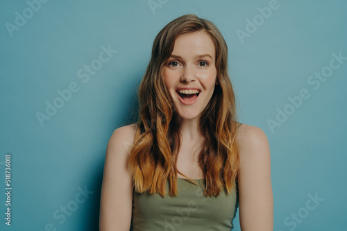 Amazed astonished young female in tank top expressing happiness and excitement, isolated on blue © VK Studio